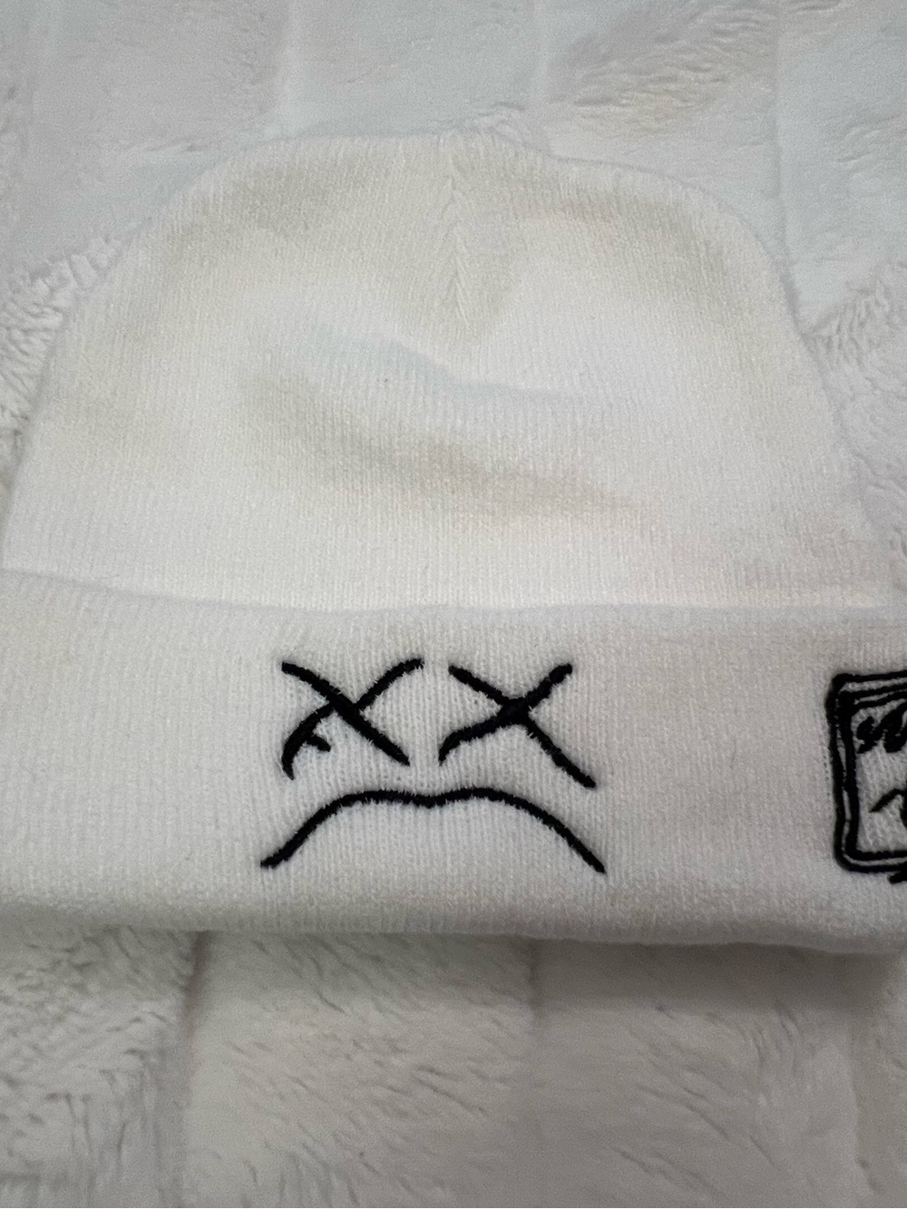 White KAWS beanie with black embroidered sad face and box logo